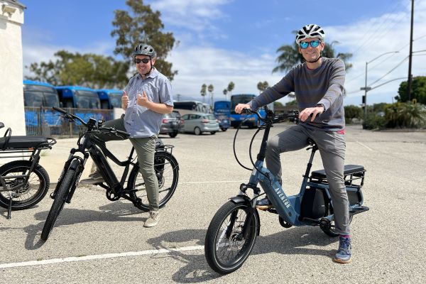 Image of Andrew Orfila and Mike Becker on Electric Bikes with Clean Air Express buses in the background.